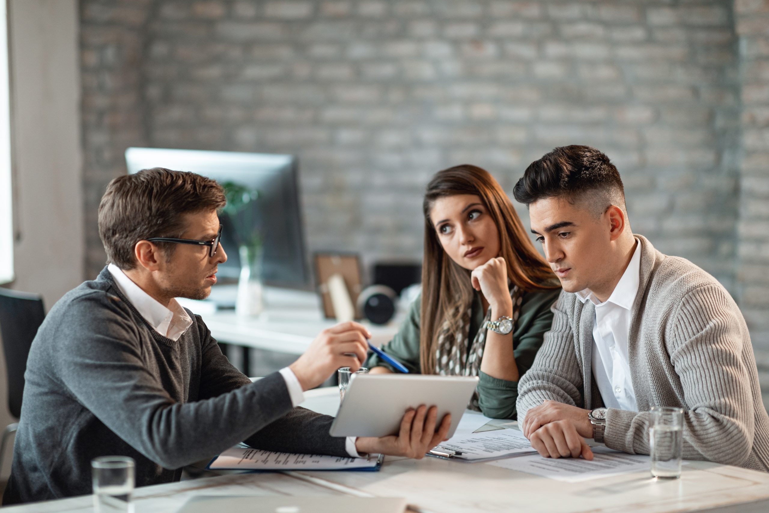 Financial advisor and young couple using touchpad on a meeting.